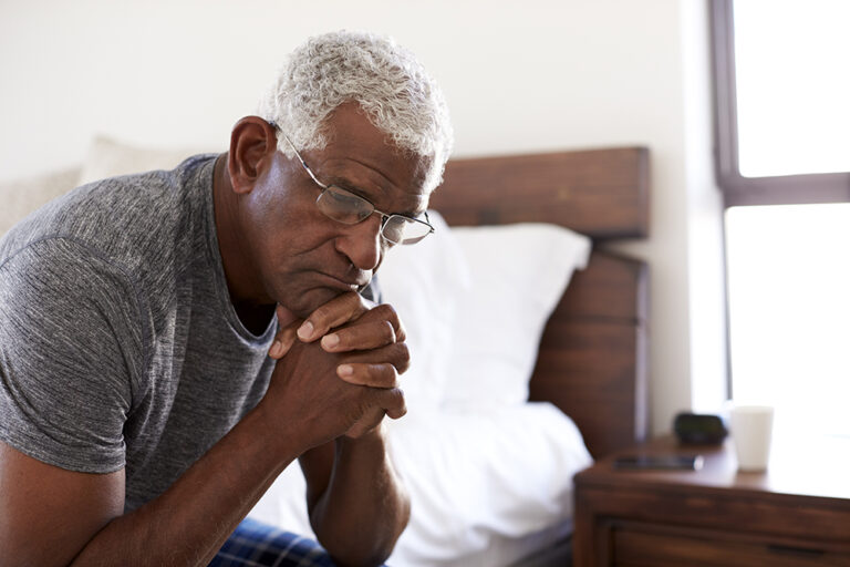 Depressed Senior Man Looking Unhappy Sitting On Side Of Bed At Home With Head In Hands